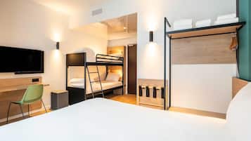 A modern hotel room with bunk beds, a desk, a chair, a TV, and a wooden shelf with towels.