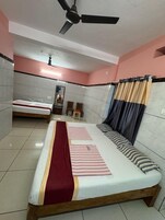 Habitación de hotel con dos camas, ventilador de techo, espejo y ventana con cortinas.