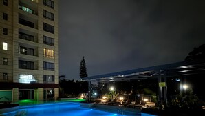A nighttime swimming pool with blue lighting, surrounded by lounge chairs and a covered area. - Alba Gardens B1102 (Nairobi)