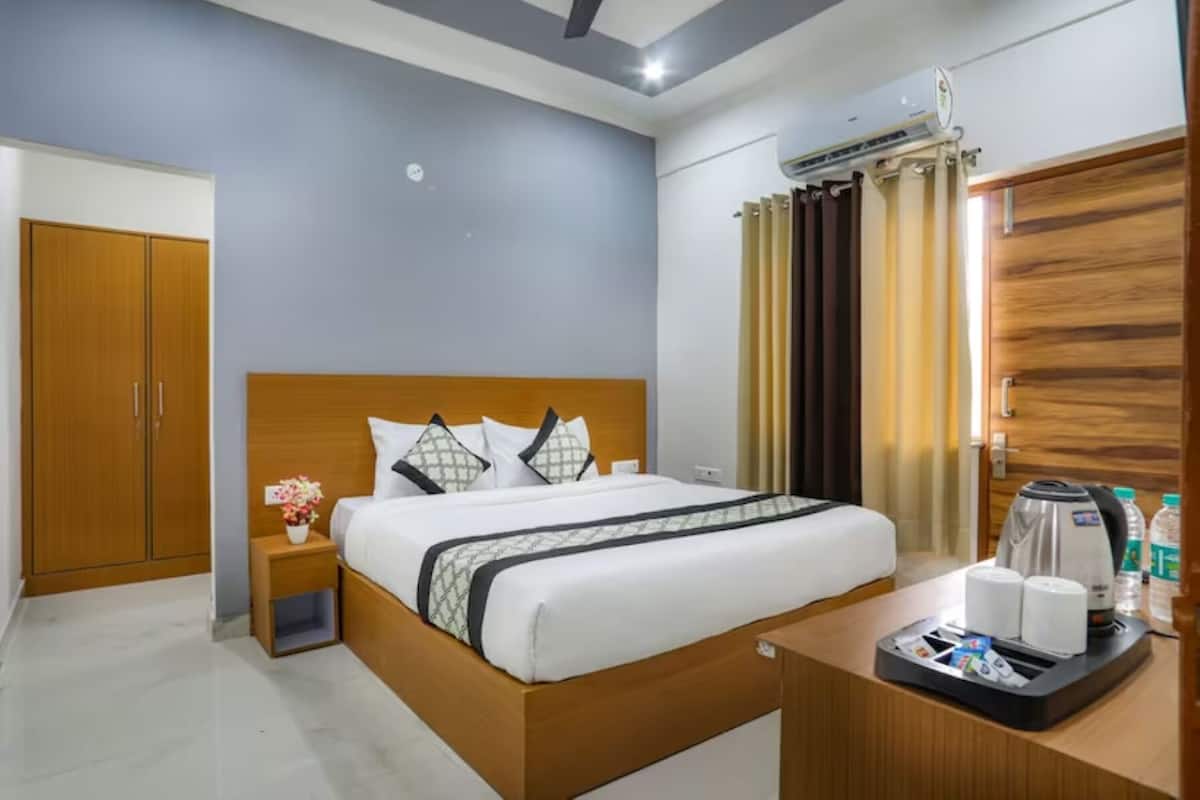 A hotel room with a wooden bed, a nightstand with a vase of flowers, a coffee maker, and a wardrobe.