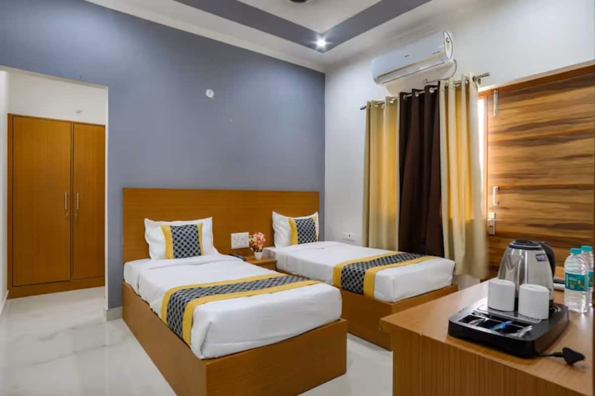 A hotel room with two beds, a wooden wardrobe, a desk with a coffee maker, and an air conditioning unit.