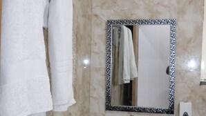 A bathroom with a marble wall, a white sink, a mirror with a black frame, and a towel hanging on the wall. - Anandam Grand (Greater Noida)