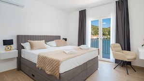 Ein modernes Schlafzimmer mit einem großen Bett, einem Nachttisch mit Lampe, einem Sessel und Blick auf einen Balkon mit Pool.