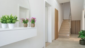 Ein moderner Flur mit weißer Wand, einer Holztreppe und Topfpflanzen auf einem weißen Beistelltisch.
