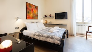 A modern bedroom with a bed, bedside tables, a TV, and a window with curtains.