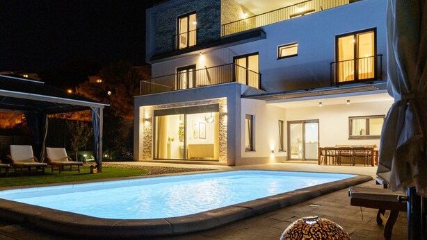 Una casa moderna a due piani con piscina, area salotto esterna e un patio ben illuminato.