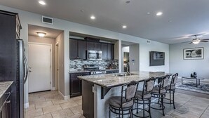 A modern kitchen with dark cabinetry, a central island with bar stools, and a dining area with a round table. - King Bed • Keyless Entry • Workspace • Fast WiFi • Chef's Kitchen • Central Loc. (Visalia)