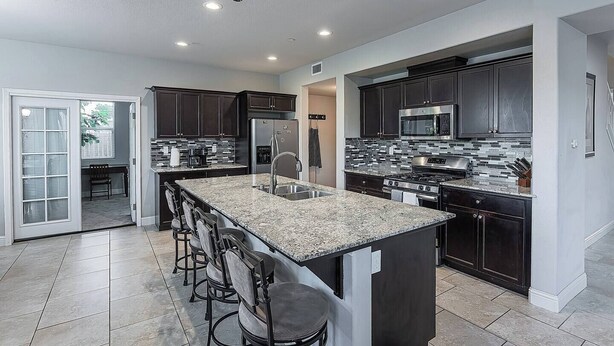 A modern kitchen with dark cabinets, granite countertops, and stainless steel appliances. - King Bed • Keyless Entry • Workspace • Fast WiFi • Chef's Kitchen • Central Loc. (Visalia)