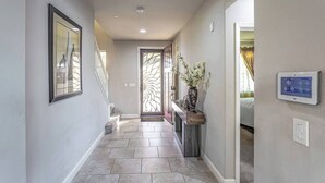 A hallway with a tiled floor, a door with a decorative glass panel, a vase with flowers on a console table, and a thermostat on the wall. - King Bed • Keyless Entry • Workspace • Fast WiFi • Chef's Kitchen • Central Loc. (Visalia)