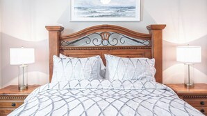 A bed with a patterned bedspread, two bedside lamps, a framed artwork above the bed, and a wooden headboard. - King Bed • Keyless Entry • Workspace • Fast WiFi • Chef's Kitchen • Central Loc. (Visalia)