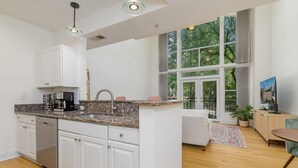 A modern kitchen with white cabinets, granite countertops, and a built-in dishwasher. There is a large window providing a view of the outdoors. - Downtown Raleigh, Pet Friendly, Close to everything. (Raleigh)