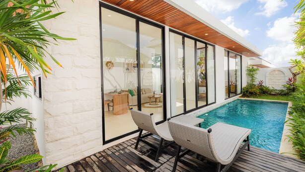 A modern outdoor pool area with a wooden deck, wicker chairs, and a glass-enclosed patio. - Kamaimo Villa (Munggu)
