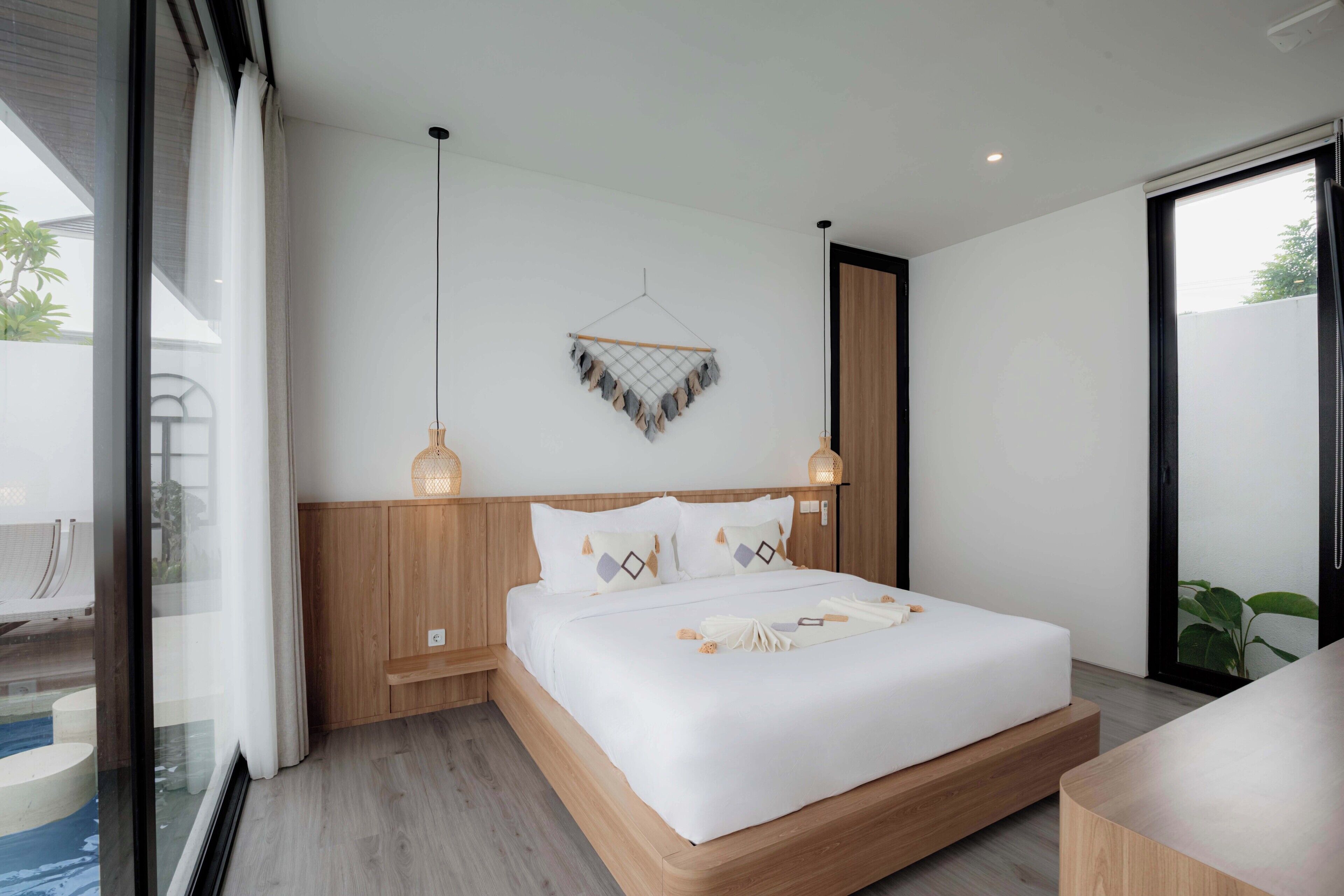 Ein modernes Schlafzimmer mit einem hölzernen Bettgestell, weißer Bettwäsche und zwei Pendelleuchten.