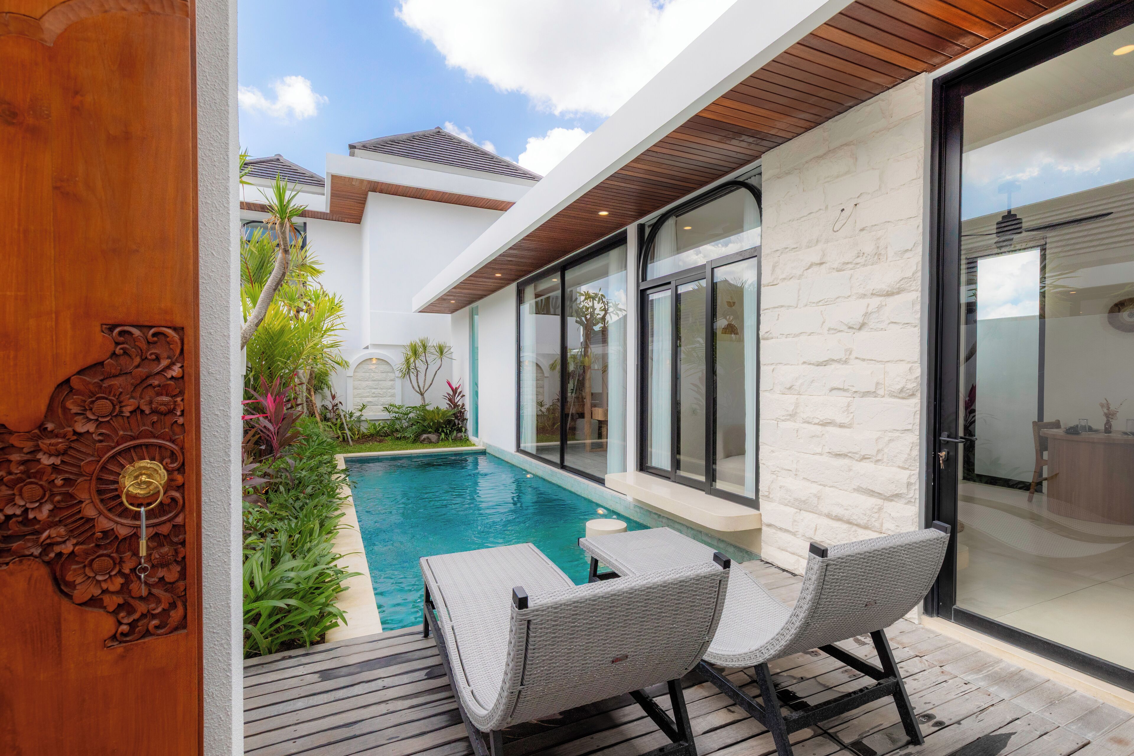 Uma área de piscina moderna ao ar livre, com duas cadeiras de vime, um deck de madeira e vista para a casa.