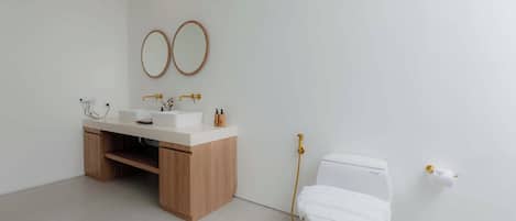 Un baño moderno con un tocador de madera, dos espejos redondos, un inodoro blanco y una ducha con detalles dorados.