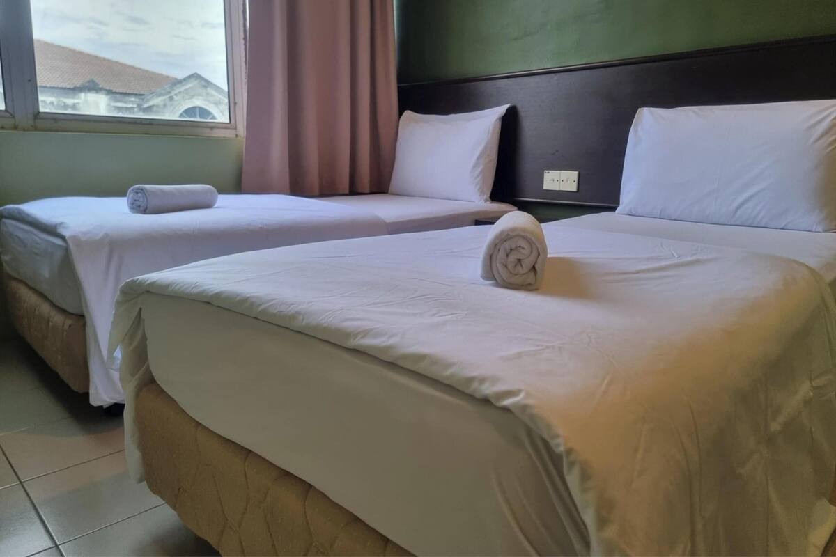 Habitación de hotel con dos camas, vistas a un edificio y una ventana con cortinas.