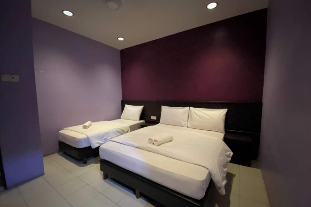 Habitación de hotel con dos camas, un cabecero oscuro y una pared de acento morada.