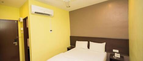 A hotel room with a bed, a nightstand, a wall-mounted air conditioner, a ceiling fan, and a door.
