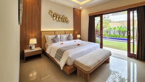 A modern hotel room with a large bed, bedside tables, a decorative wall piece, and a view of the garden through a sliding door. - AYUR Bali Villas by Nagisa Bali (Kerobokan)