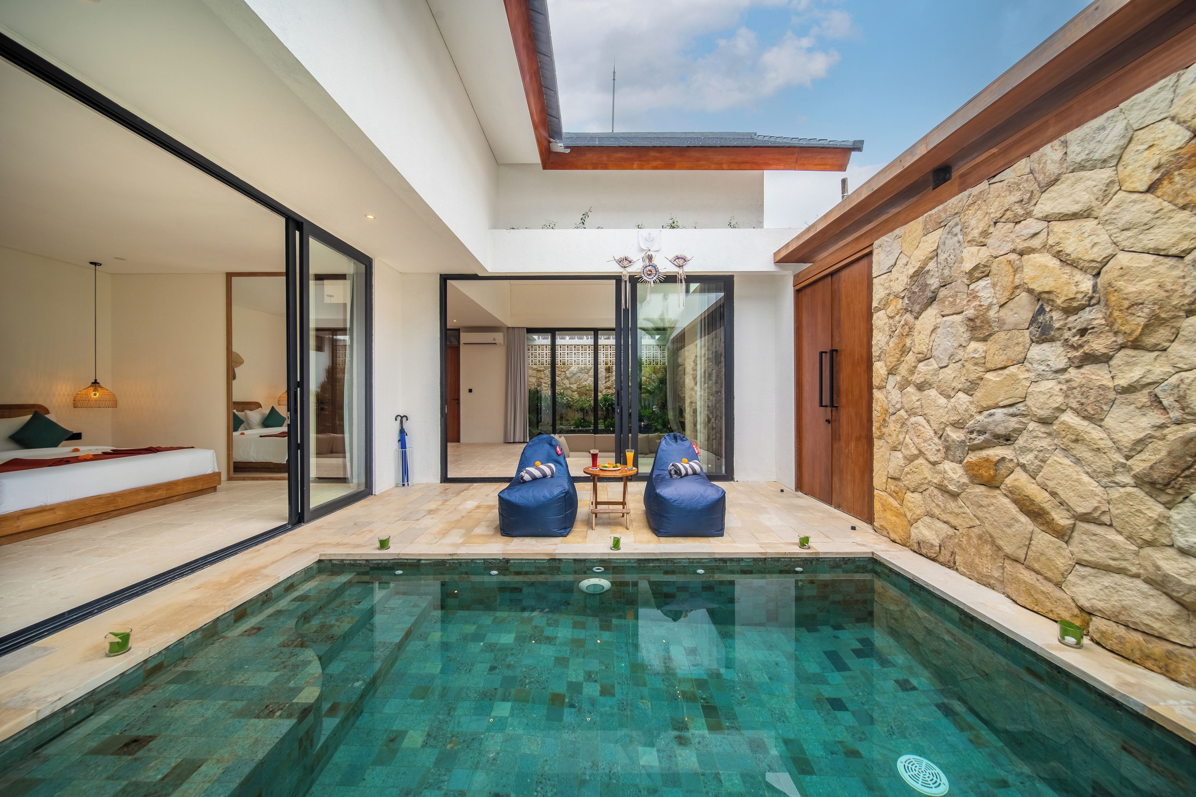 A modern pool area with a stone wall, two blue bean bags, and a view of the outdoors.