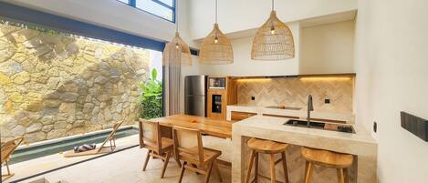 A modern kitchen with a stone wall, wooden furniture, and pendant lighting.