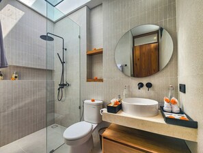 A modern bathroom with a glass-enclosed shower, a white toilet, and a large round mirror above a sink with a wooden countertop. - AYUR Bali Villas by Nagisa Bali (Kerobokan)
