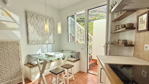 A kitchen with a glass dining table, white cabinets, and a view of a mountainous landscape through the window. - Casa Ale, endless sea view ! (Las Aguas)