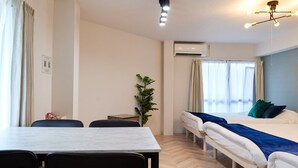 A hotel room with a bed, a desk, and chairs. There is a plant and an air conditioning unit on the wall. - XS41 XROSS STAY Juso1 (大阪市淀川区十三東)