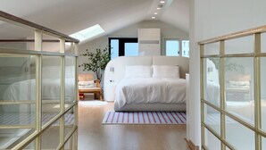 Un dormitorio moderno con tragaluz, una cama grande, una silla y vistas al exterior.
