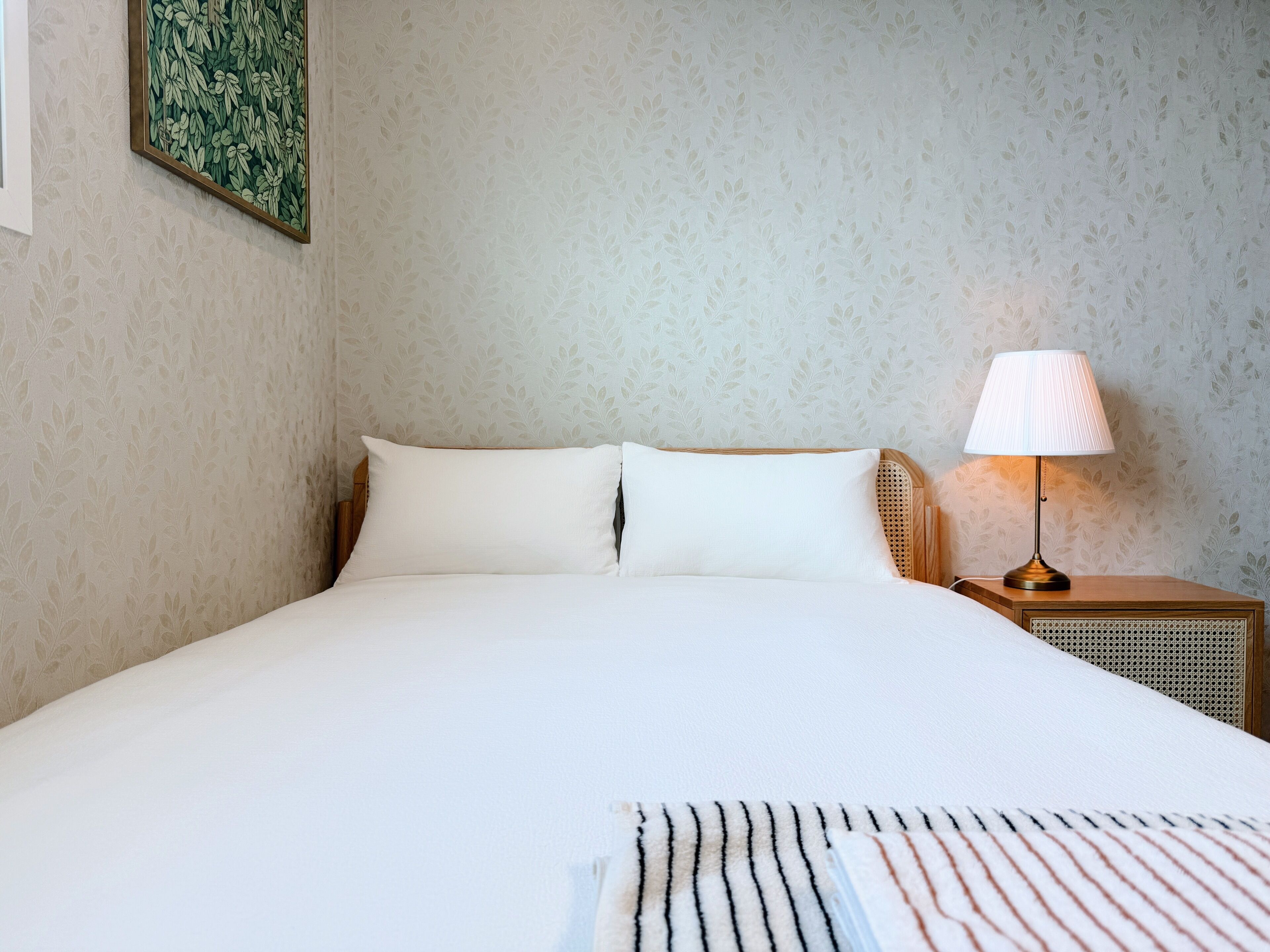 A neatly made bed with white linens, a bedside lamp, and a framed artwork on the wall.