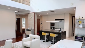 Una cocina moderna con una isla central, taburetes de bar y un comedor con una mesa de vidrio.