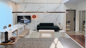 Una sala de estar moderna con un televisor de pantalla plana, un ventilador de techo, un sofá verde, un sillón blanco y una estación de café.