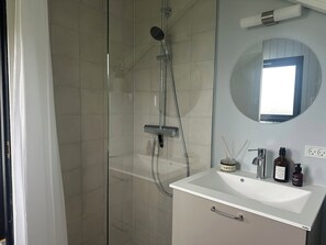 Une salle de bain moderne avec une douche à parois de verre, un lavabo blanc et un miroir rond placé au-dessus.