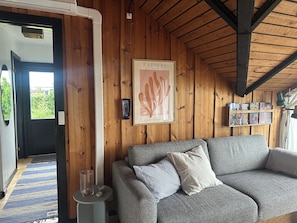A cozy room with a grey sofa, a framed poster on the wall, and a bookshelf with books.