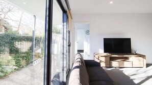 Un salon moderne doté d’une grande fenêtre, d’un téléviseur à écran plat et d’un meuble de rangement en bois pour les appareils multimédias.