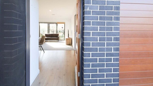 Un intérieur moderne avec un mur en briques, un lambris en bois et une vue sur un espace de vie comprenant un canapé et une table.