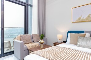 A modern hotel room with a large window, a sofa, a bed, and a nightstand with a lamp. - Bloomfields Studio in The Gate-Masdar (Abu Dhabi)