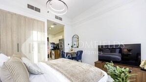A modern bedroom with a bed, bedside table, TV, and a view into the kitchen. - Bloomfields Comfort Stu The Gate  (Abu Dhabi)