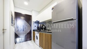 A modern kitchen with a stainless steel refrigerator, a washing machine, and a tiled backsplash. - Bloomfields Comfort Stu The Gate  (Abu Dhabi)