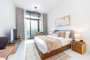 A modern hotel room with a large bed, a TV, a desk, and a view of the city. - Bloomfields Studio in The Gate-Masdar (Abu Dhabi)