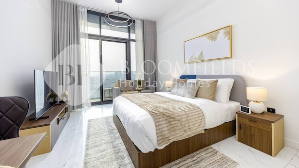 A modern hotel bedroom with a large bed, a TV, a desk, and a view of the city. - Bloomfields Comfort Stu The Gate  (Abu Dhabi)