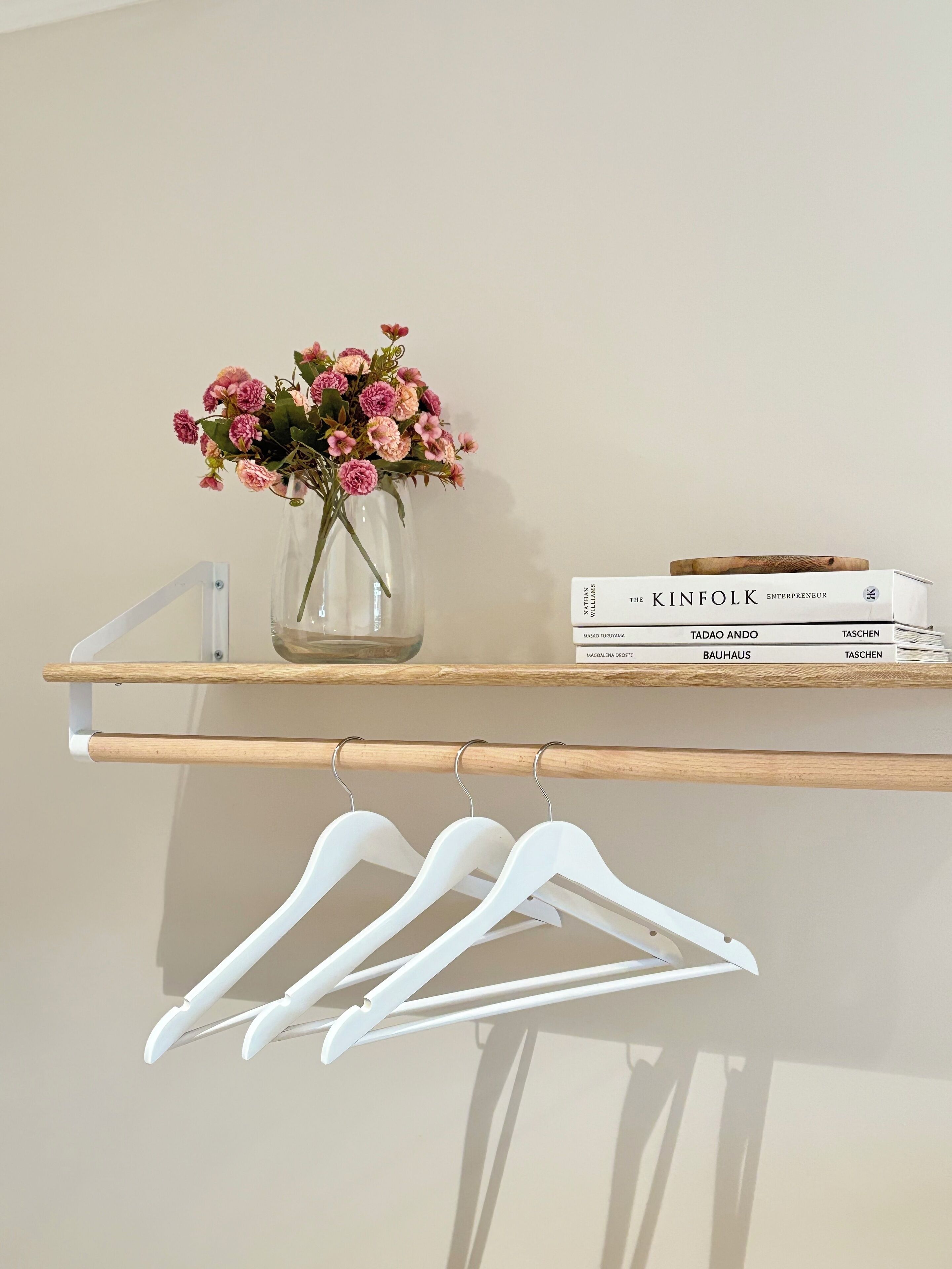 A shelf with a vase of flowers, a stack of books, and white hangers.