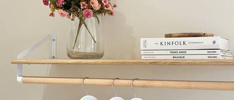 A shelf with a vase of flowers, a stack of books, and white hangers.