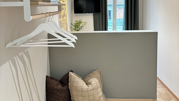 A modern room with a wooden bench, a wall-mounted TV, and a window with curtains. - Hôtel mi corazon (Paris)