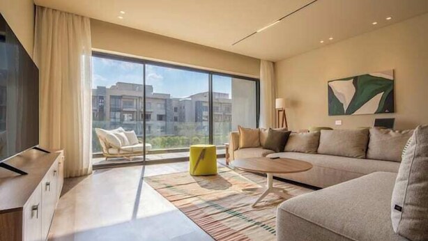 A modern living room with a sofa, coffee table, and a view of the city through large windows. - Kennah Meraviglia | Lake View Residence, New Cairo (New Cairo)