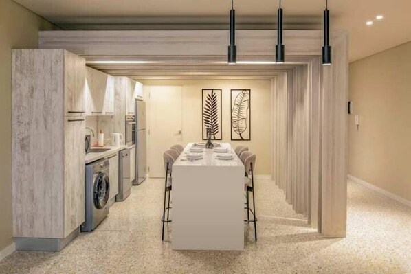 A modern kitchen with a built-in washing machine, a dining area with a long table, and pendant lighting. - Kennah Meraviglia | Lake View Residence, New Cairo (New Cairo)
