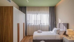 A hotel room with two beds, a wooden wardrobe, a large window with curtains, and a bedside lamp. - Kennah Meraviglia | Lake View Residence, New Cairo (New Cairo)