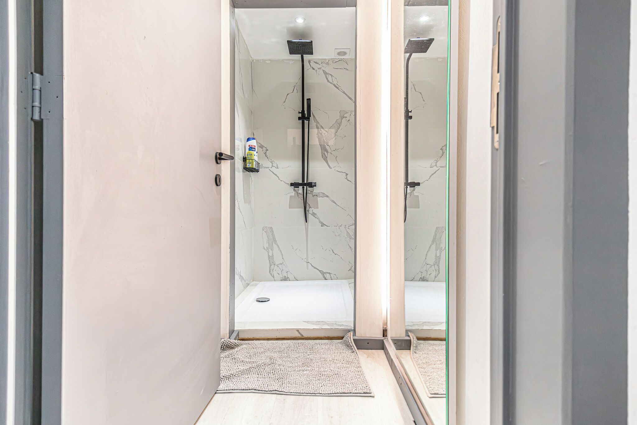 A modern bathroom with a glass shower enclosure, marble walls, and a visible bottle of shampoo.