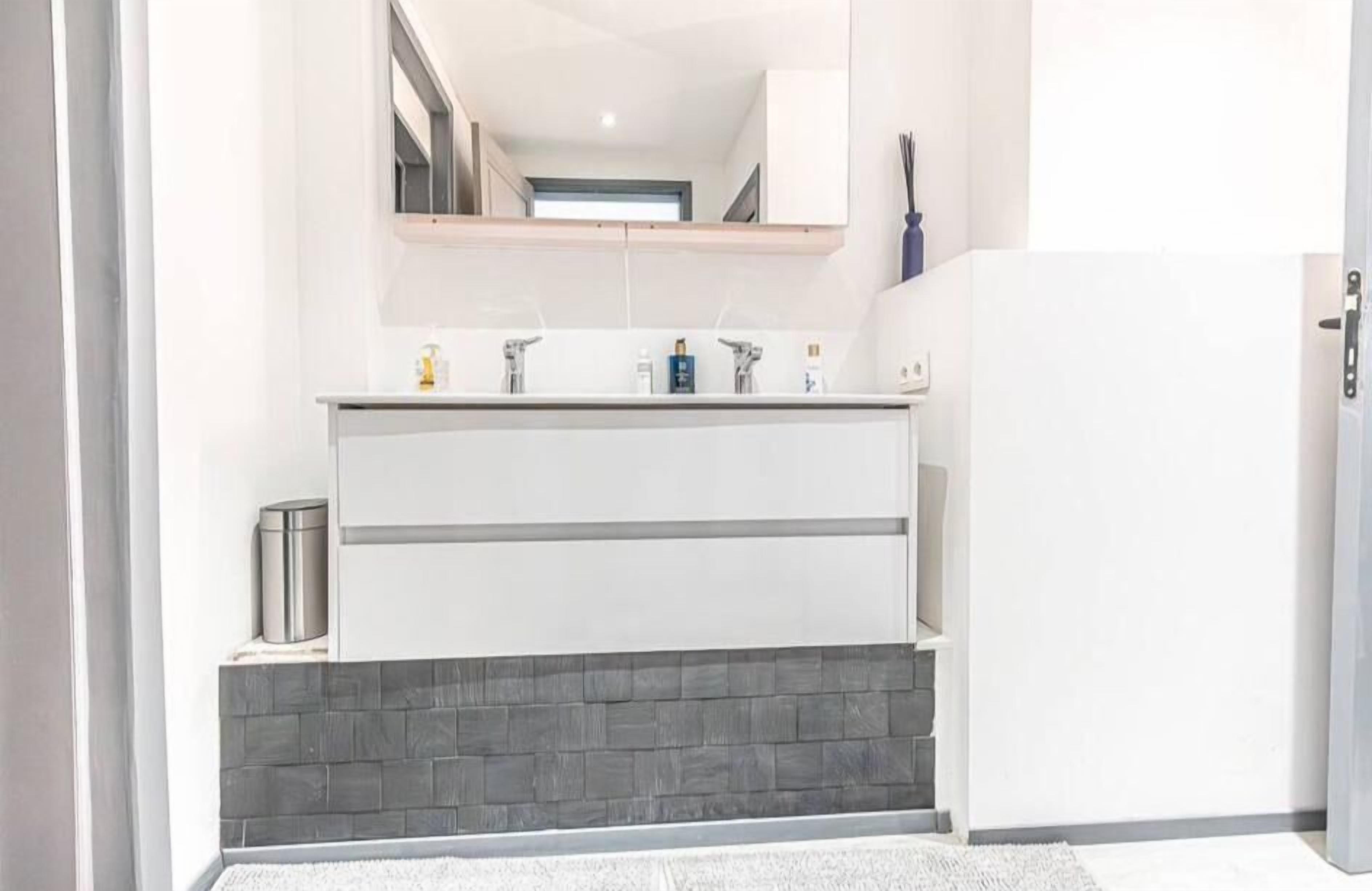 A modern bathroom with a white vanity, a mirror, and a tiled backsplash.