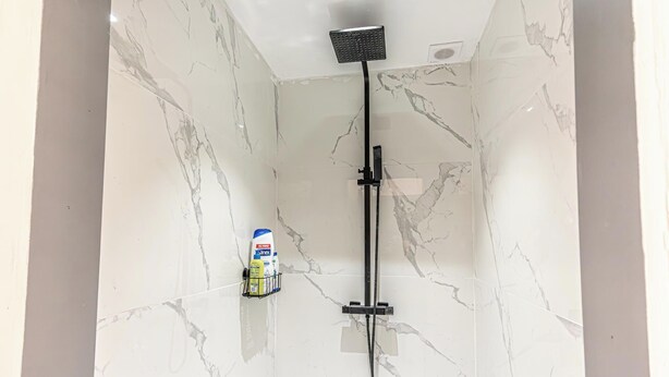 A bathroom with a shower, marble walls, and a bottle of shampoo on a shelf. - Comfy 5BR Apartment in Heart of Ghent (Ghent)